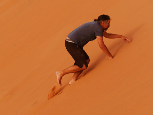 Mann läuft in der Erg Chebbi auf allen Vieren eine Düne hoch