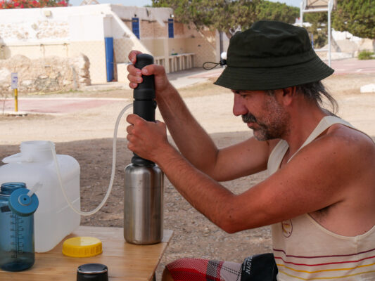 Mann pumpt Wasser durch den Filter in eine Trinkflasche