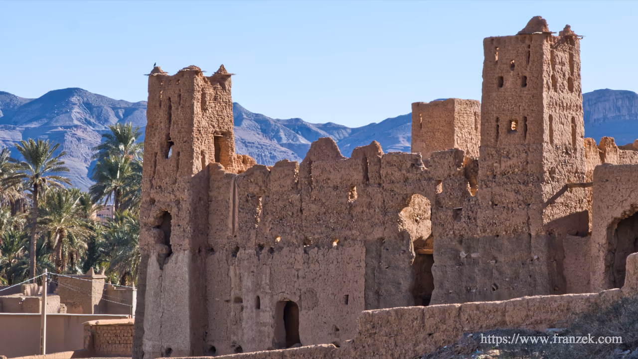 Süd-Marokko Mietwagen-Route: Kosten & Tipps (Anti-Atlas) 51 Ruine einer alten Lehm-Kasbah in N’Kob. Die Mauern sind teilweise eingestürzt und geben durch die Fensteröffnungen und Risse den Blick auf das dahinterliegende bläuliche Gebirge frei.
