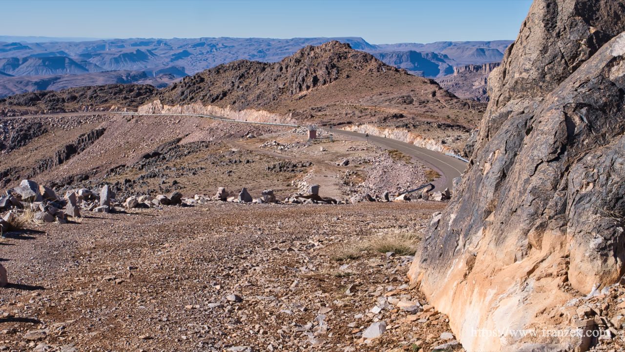 Süd-Marokko Mietwagen-Route: Kosten & Tipps (Anti-Atlas) 57 Eine kurvenreiche Asphaltstraße schlängelt sich durch die karge, dunkle Berglandschaft des Jbel Saghro unter blauem Himmel.