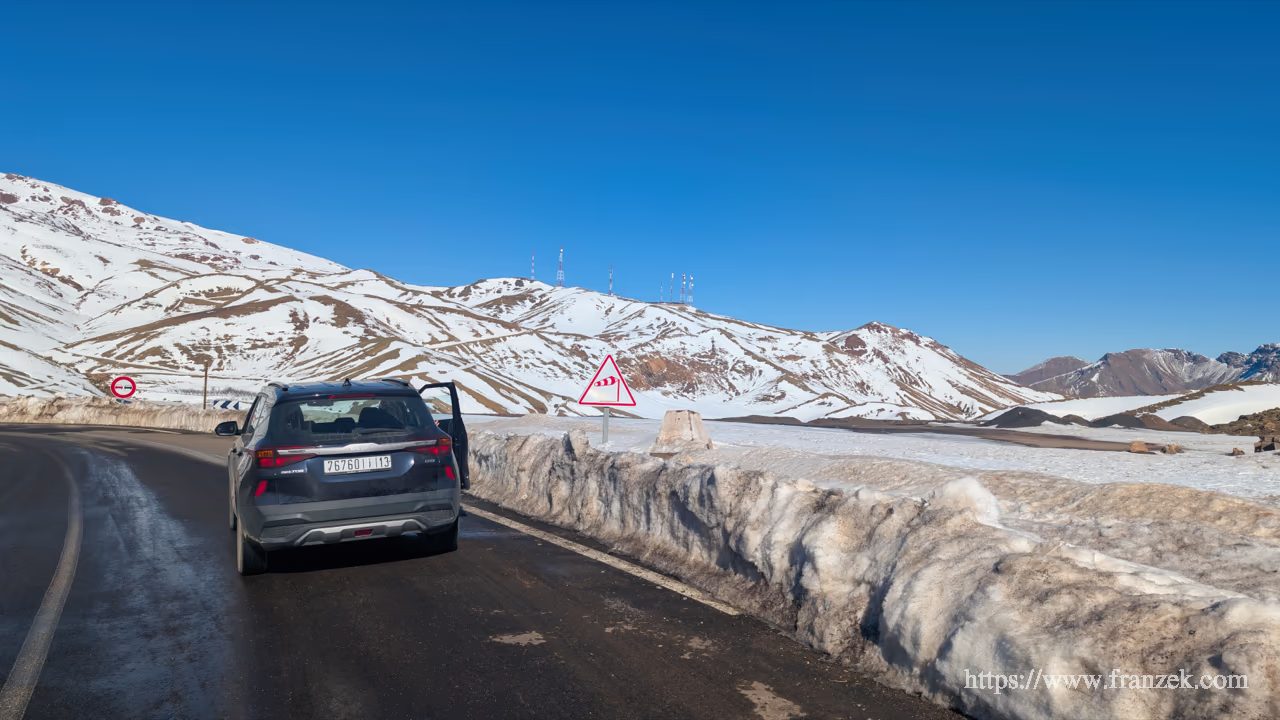 Süd-Marokko Mietwagen-Route: Kosten & Tipps (Anti-Atlas) 66 Ein dunkler SUV parkt auf der Passstraße des Tizi n'Tichka. Die gesamte Berglandschaft ist tief verschneit, hohe Schneewände säumen den Straßenrand. Im Hintergrund ragen die Gipfel des Hohen Atlas unter einem strahlend blauen Himmel auf.