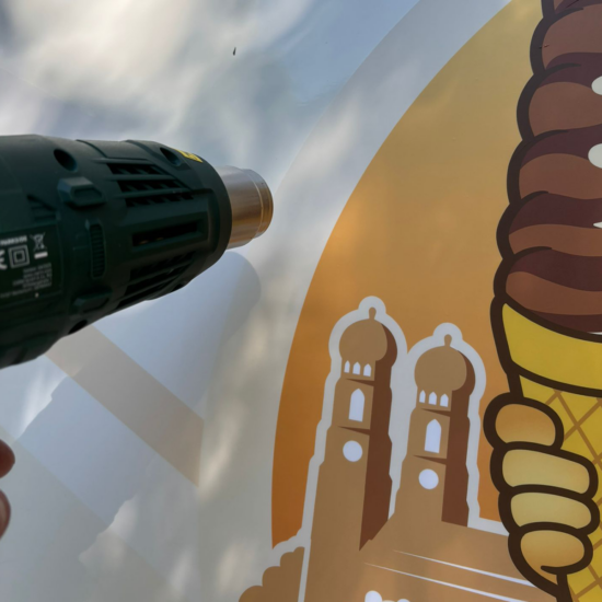 Kastenwagen selbst folieren: Dein Guide fürs Fahrzeugbranding 17 Heißluftföhn erwärmt die Folie mit dem München-Motiv zum Einarbeiten in die Fläche